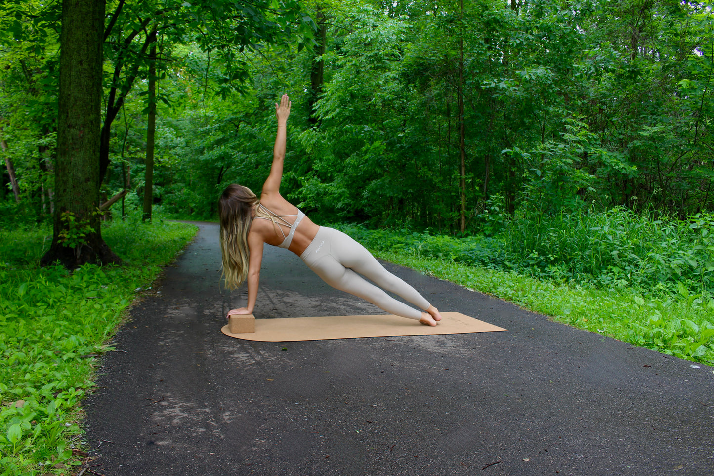 Woman performing side plank on a cork yoga mat with cork yoga blocks placed nearby.