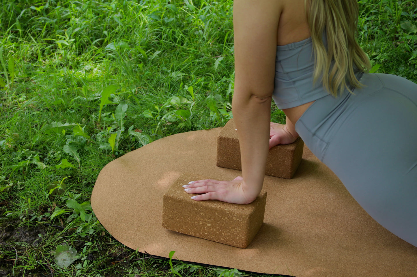 Cork yoga block in use during an outdoor yoga session on a cork yoga mat in a grassy area.