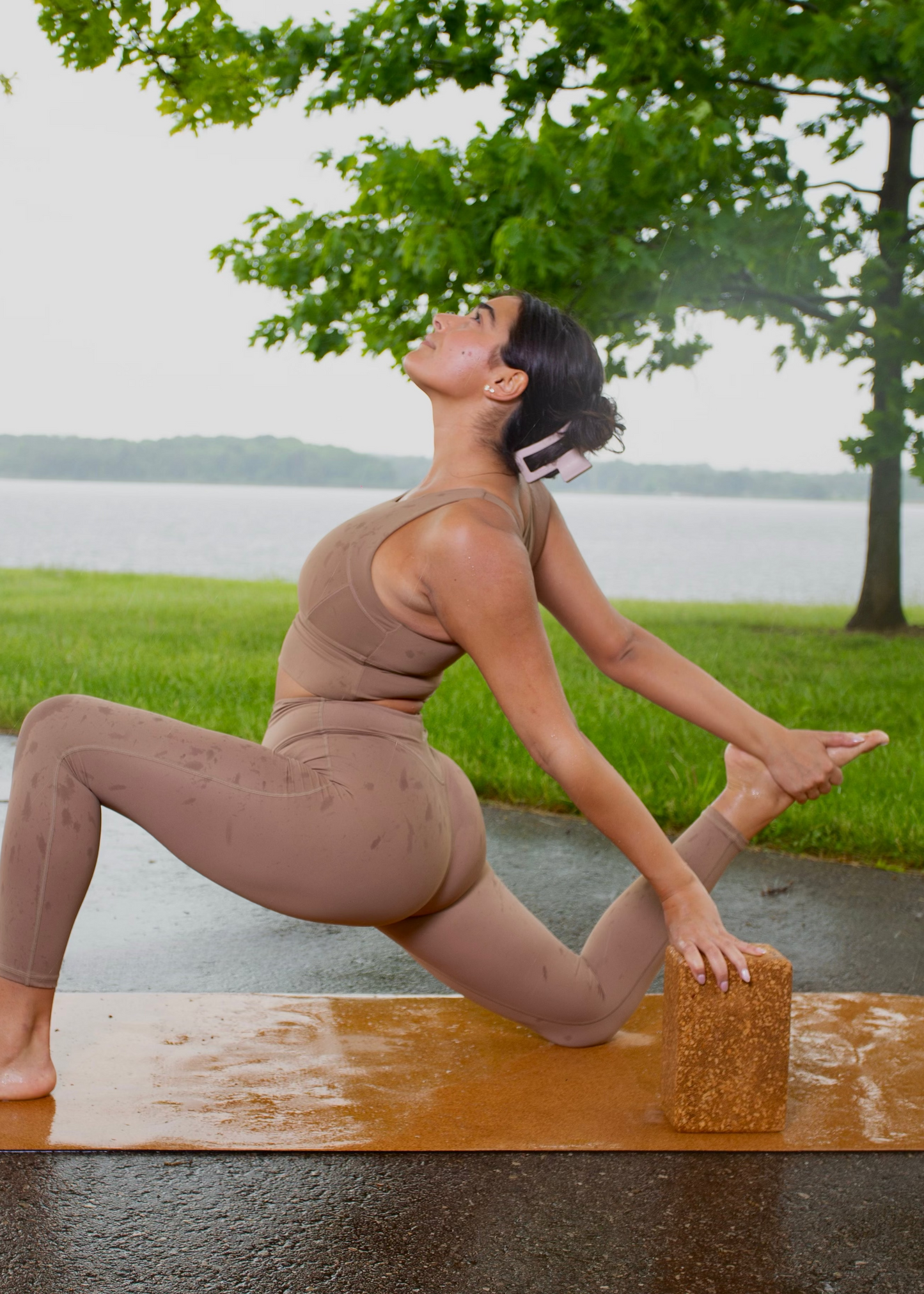 Woman performing a deep lunge stretch on a cork yoga mat, using a cork yoga block under her hand for balance during an outdoor session by the lake.