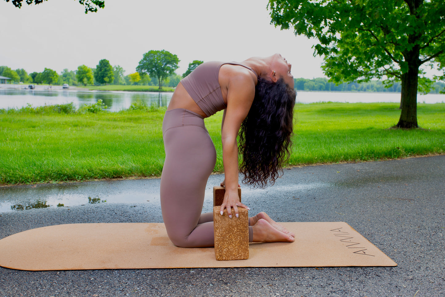 Woman in a seated yoga stretch on a cork yoga mat outdoors, wearing a taupe activewear set.