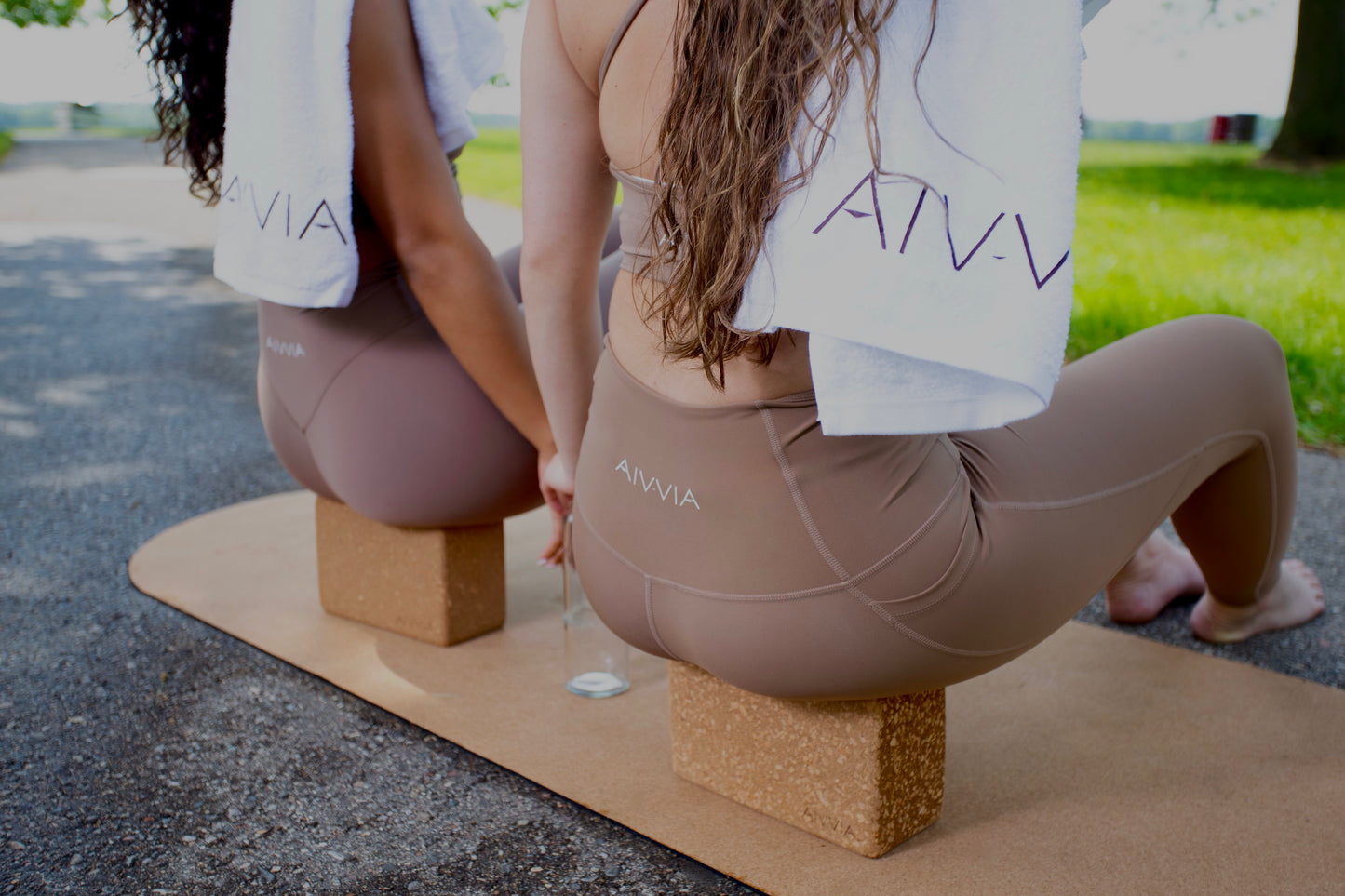 Close-up of two women sitting on cork yoga mats, using yoga blocks for seated posture support.