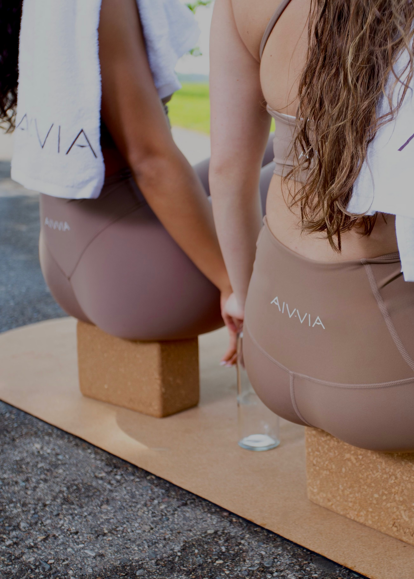 Close-up of two women sitting on cork yoga mats, using yoga blocks for seated posture support.
