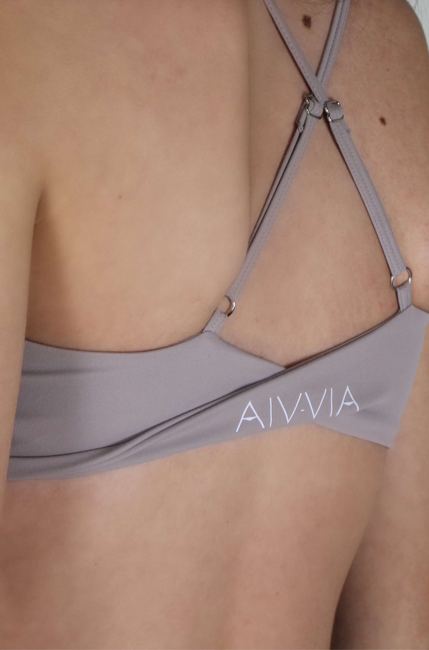 Close-up of light taupe Aivvia Athletics sports bra featuring thin criss-cross straps and back logo detail.