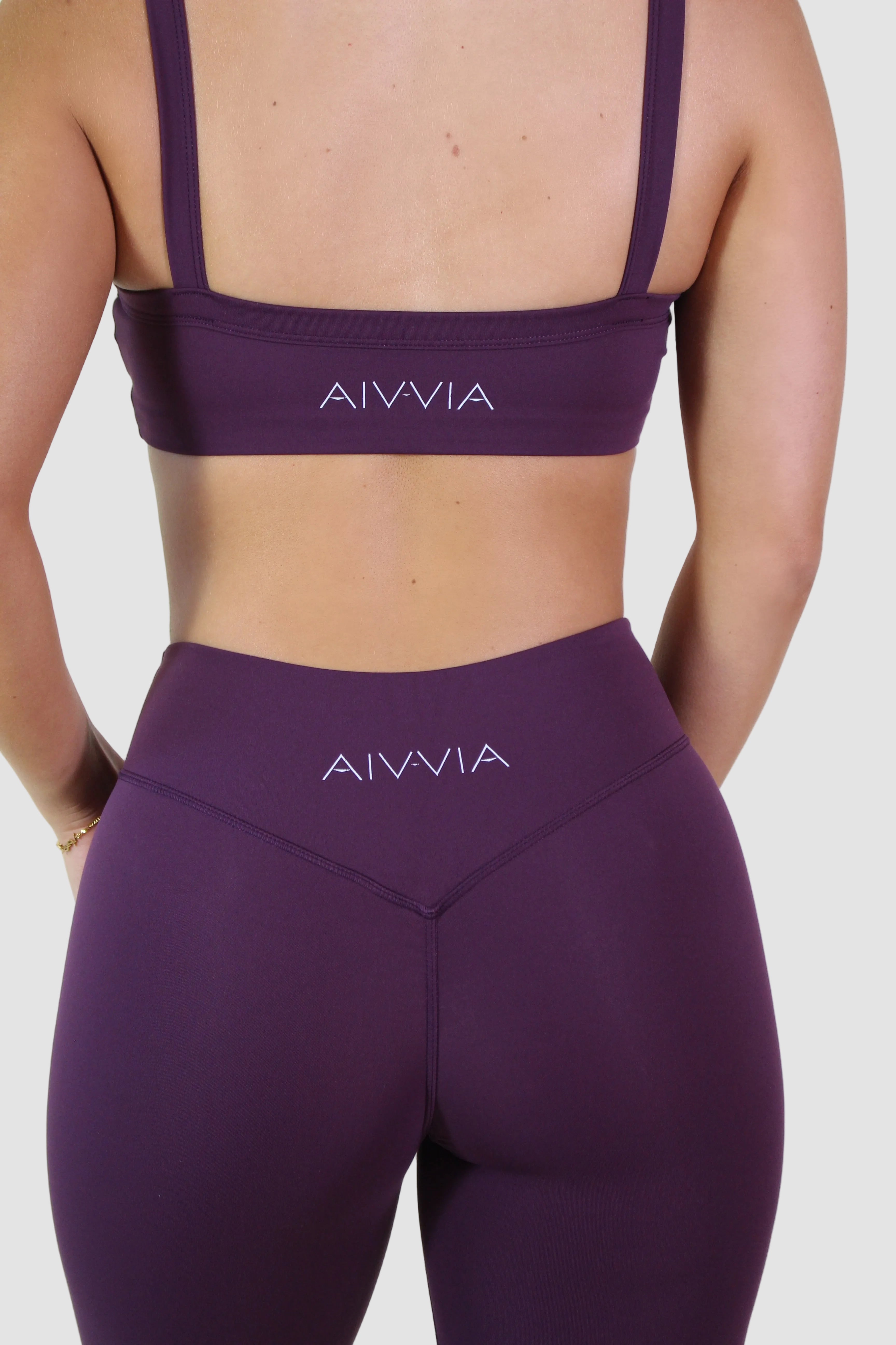 Person wearing purple sports bra and leggings with 'AIVVIA' branding on a white background