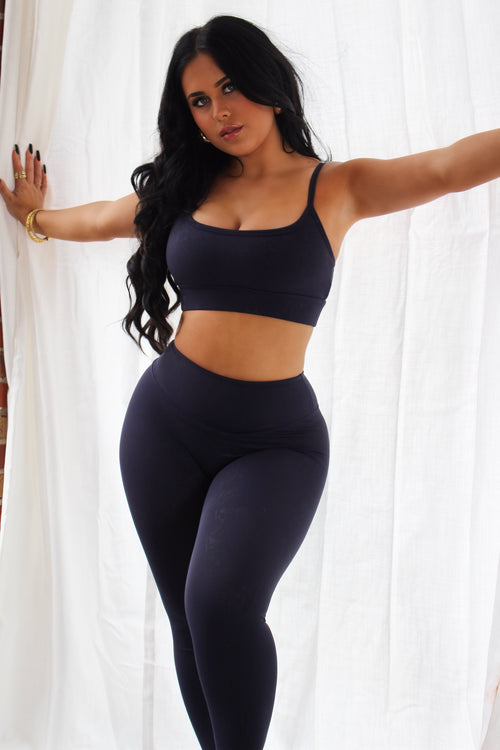 Woman wearing navy Aivvia Athletics high-waisted leggings and matching sports bra, sleek fit for training or yoga.