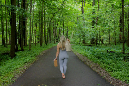 Woman walking down a forest path carrying cork yoga blocks and a rolled mat.