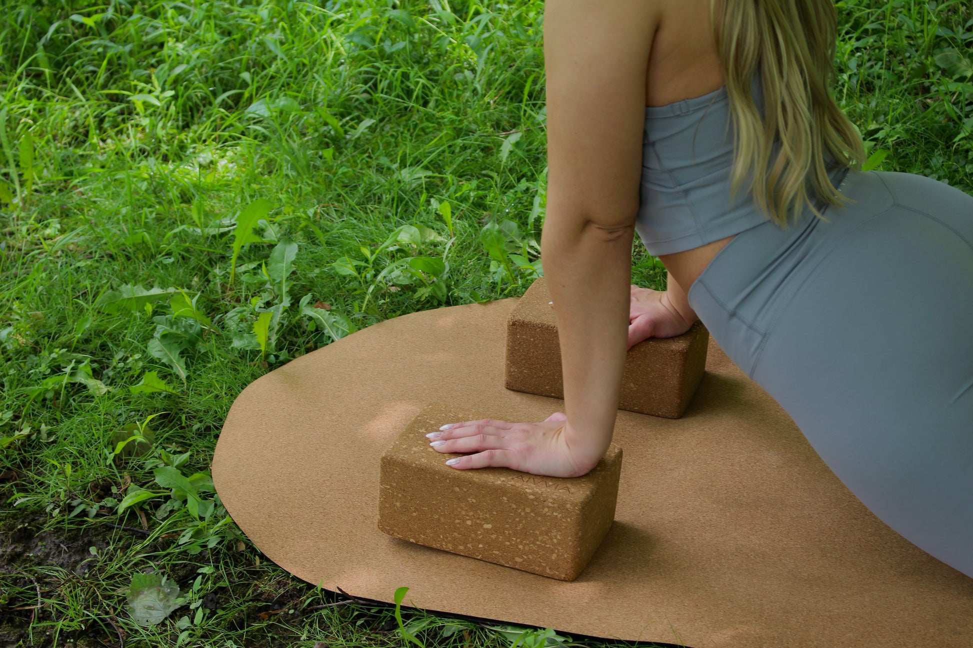 Cork yoga block in use during an outdoor yoga session on a cork yoga mat in a grassy area.