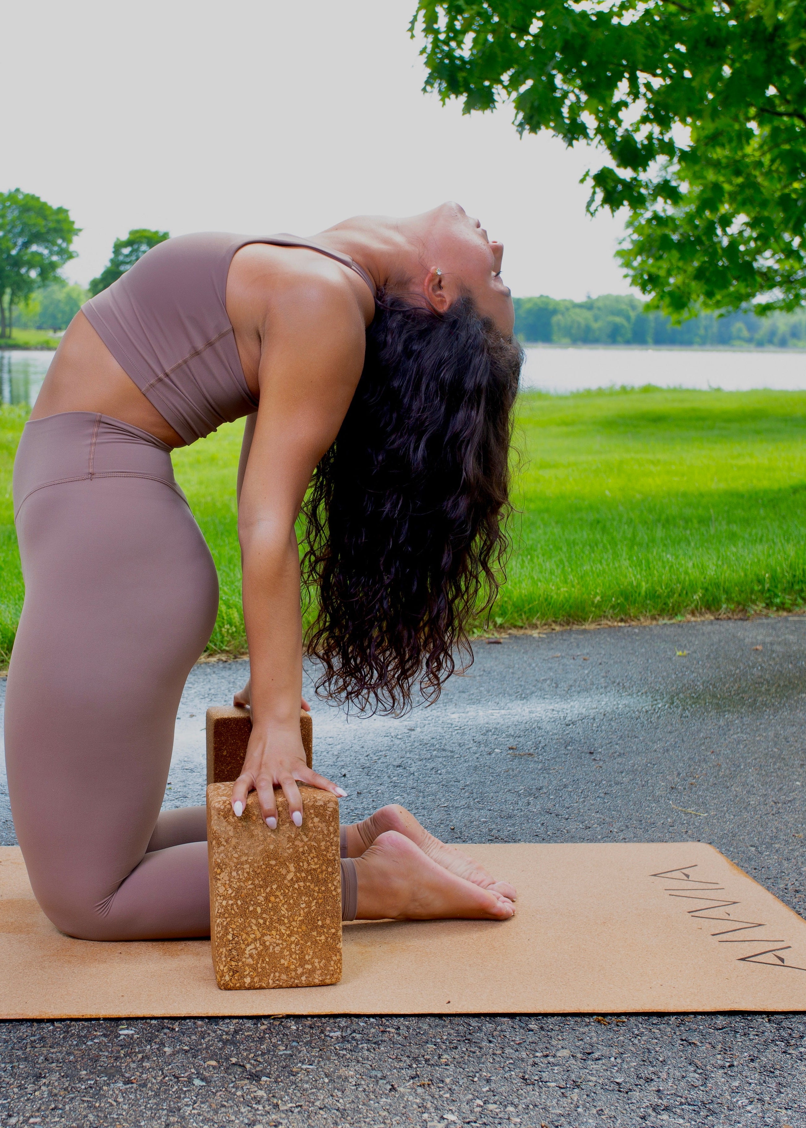 Woman in a seated yoga stretch on a cork yoga mat outdoors, wearing a taupe activewear set.