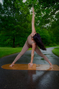 Woman performing triangle pose on a cork yoga mat with yoga blocks, surrounded by greenery.