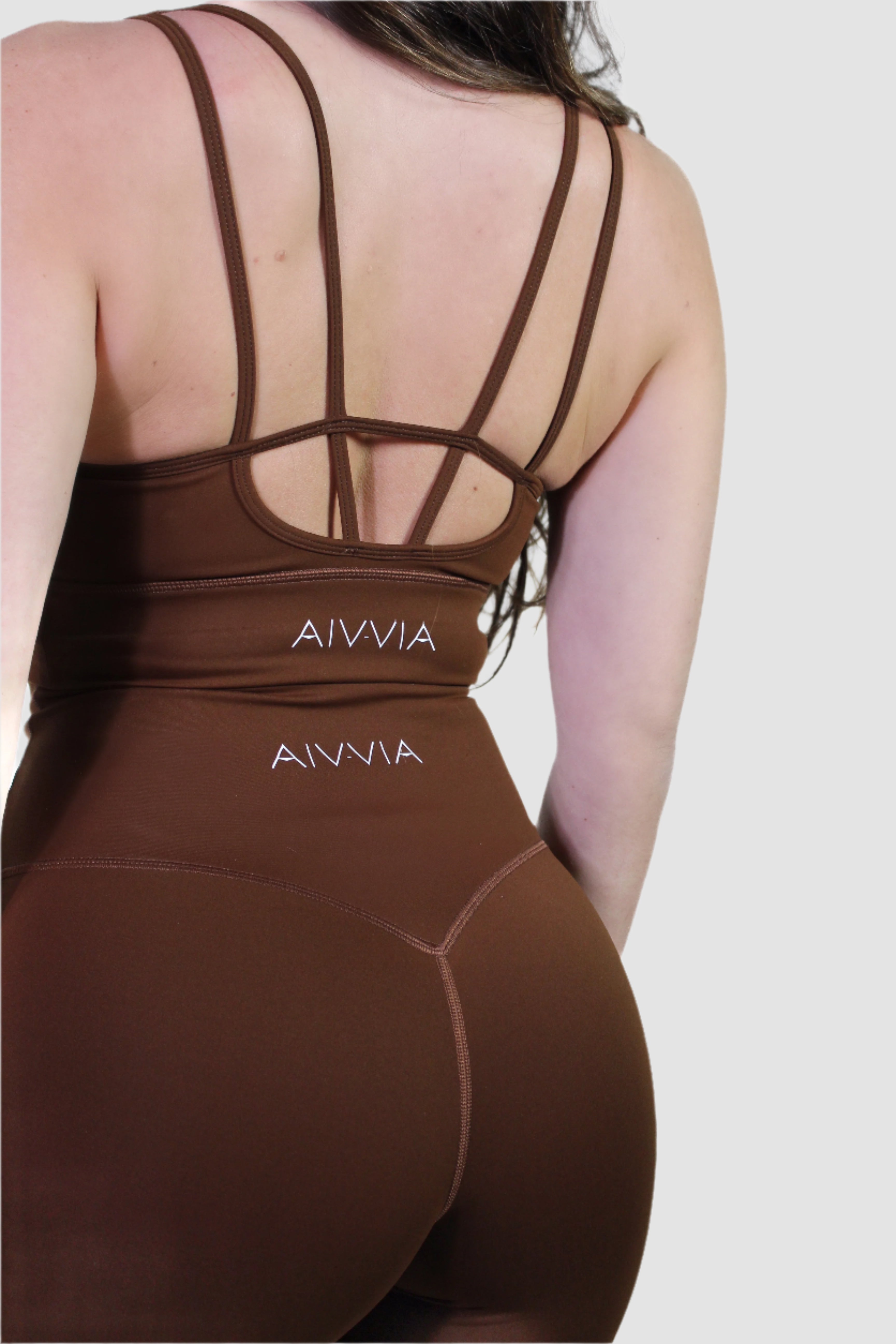 Back view of the chocolate brown activewear set, showing strappy sports bra detail and logo on the waistband of the shorts.