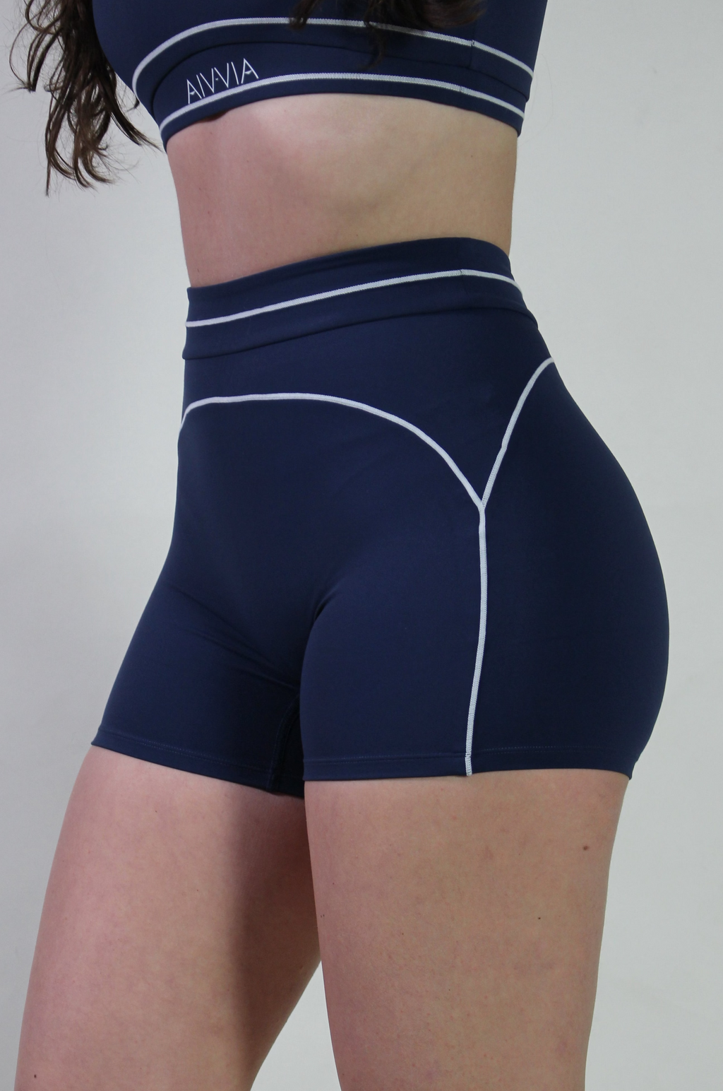 Side profile of model Annessa in Midnight Navy Sculpt Shorts showing the high-waisted fit and white piping along the hip.