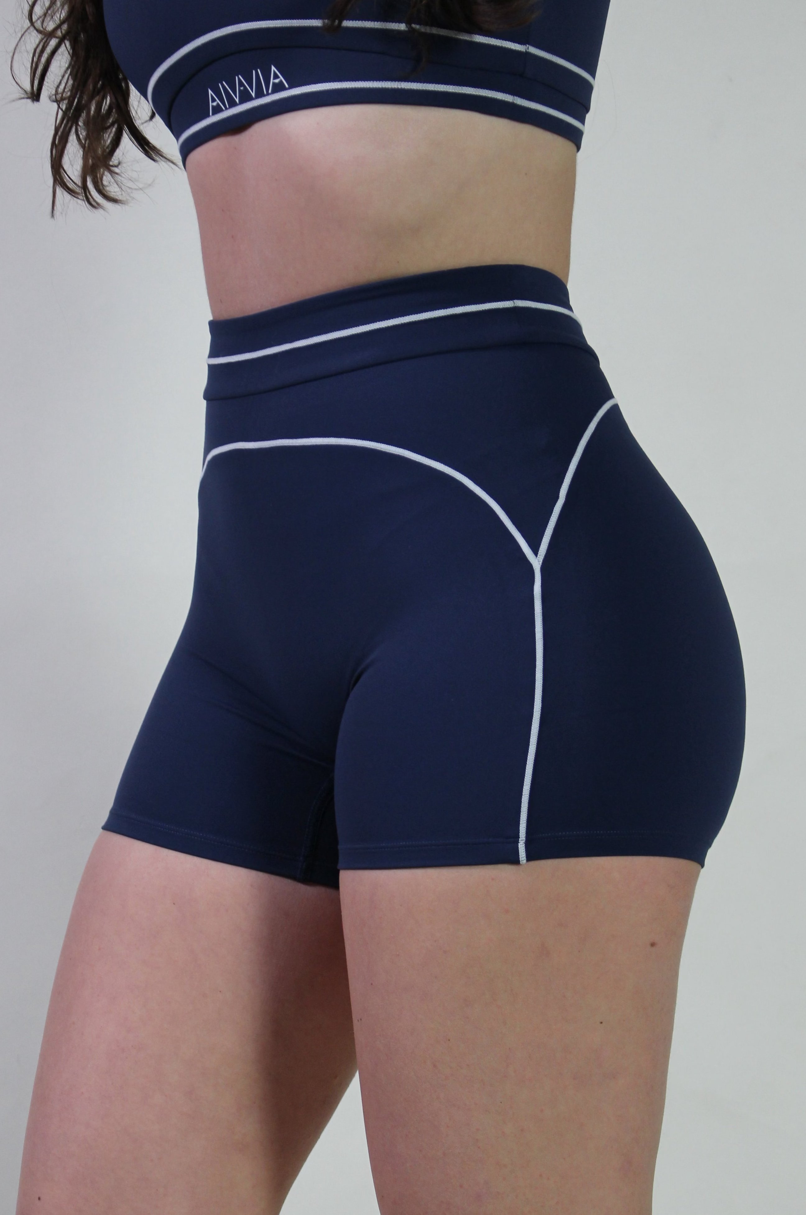 Side profile of model Annessa in Midnight Navy Sculpt Shorts showing the high-waisted fit and white piping along the hip.