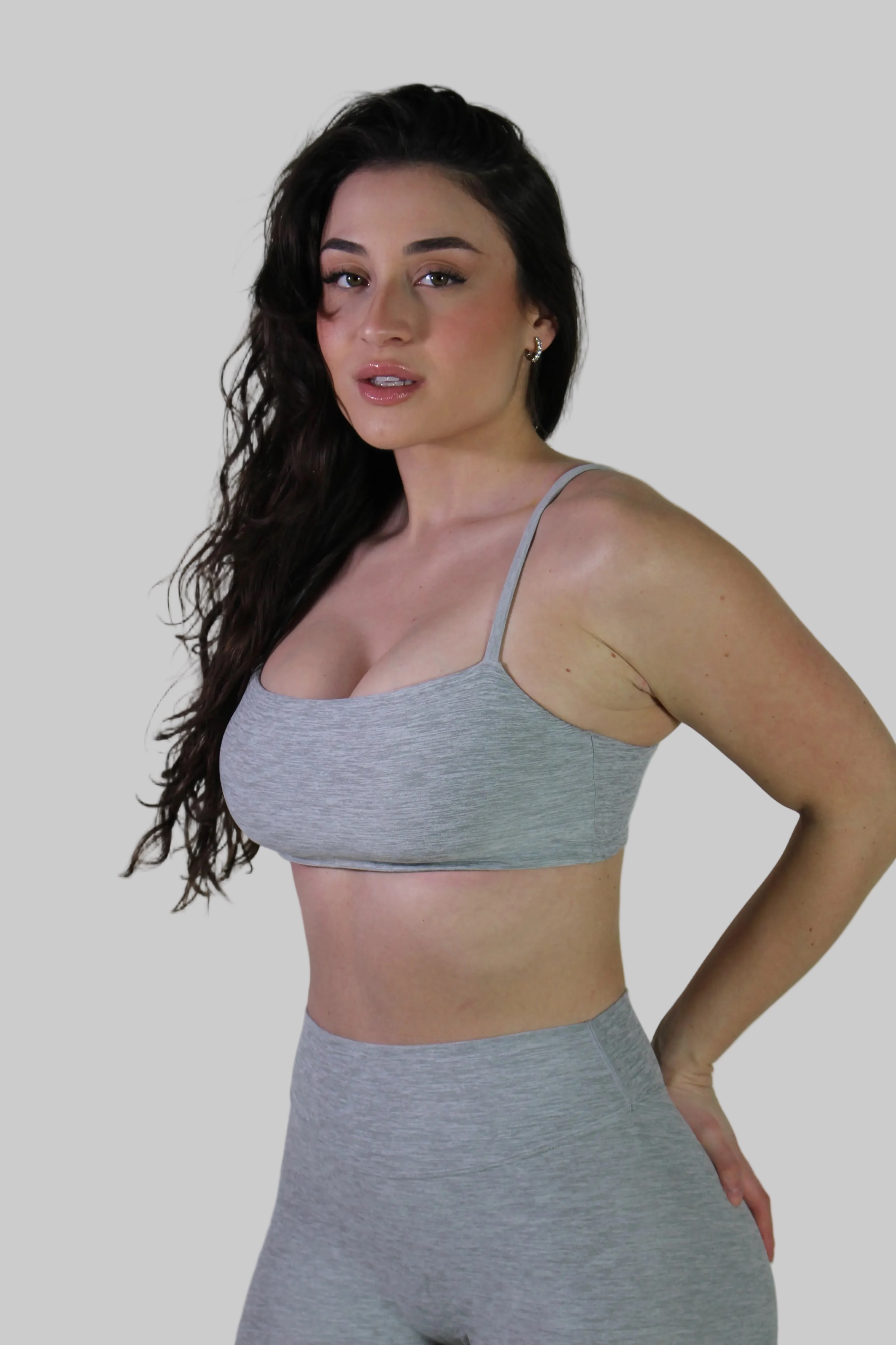 Front angled side view of a woman wearing Aivvia Athletics gray sports bra on plain background
