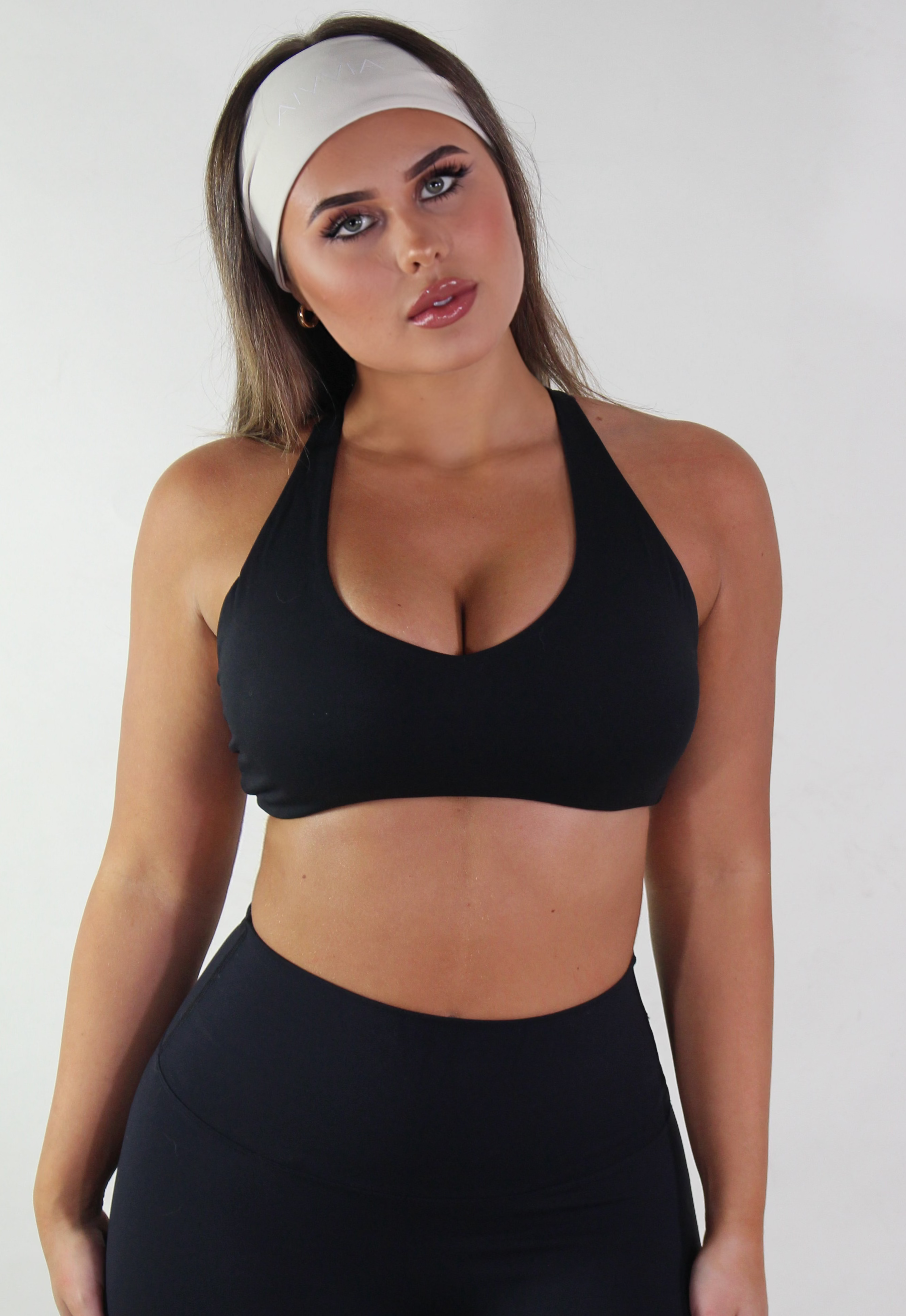 Woman wearing a black sports bra and leggings with a white headband on a plain background