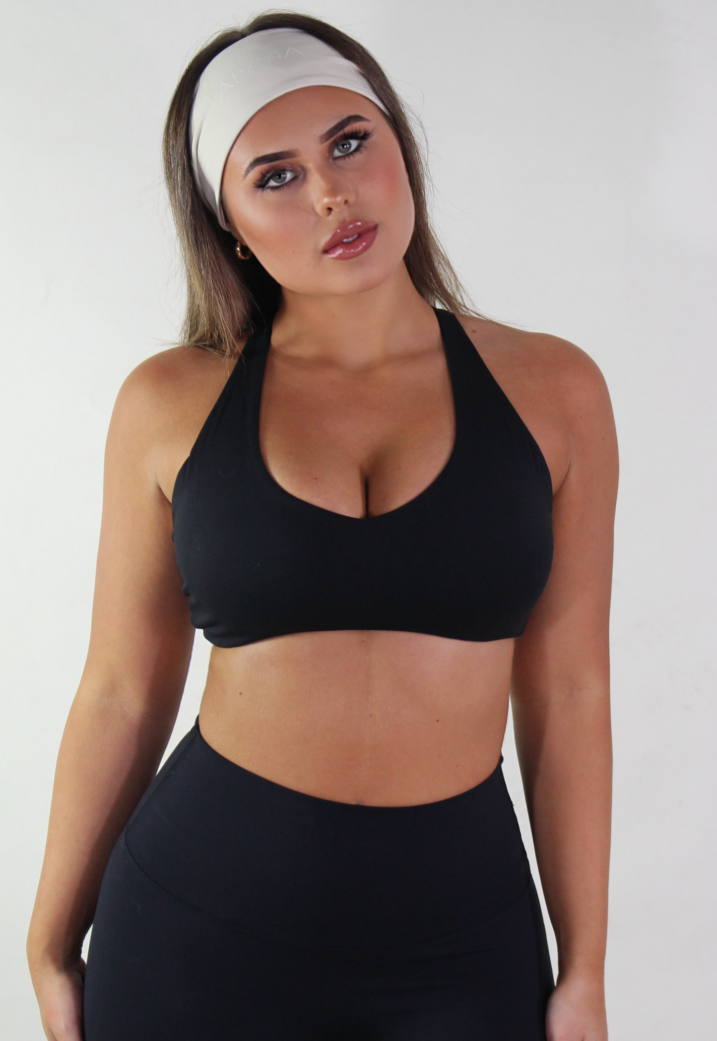 Woman wearing a black sports bra and leggings with a white headband on a plain background