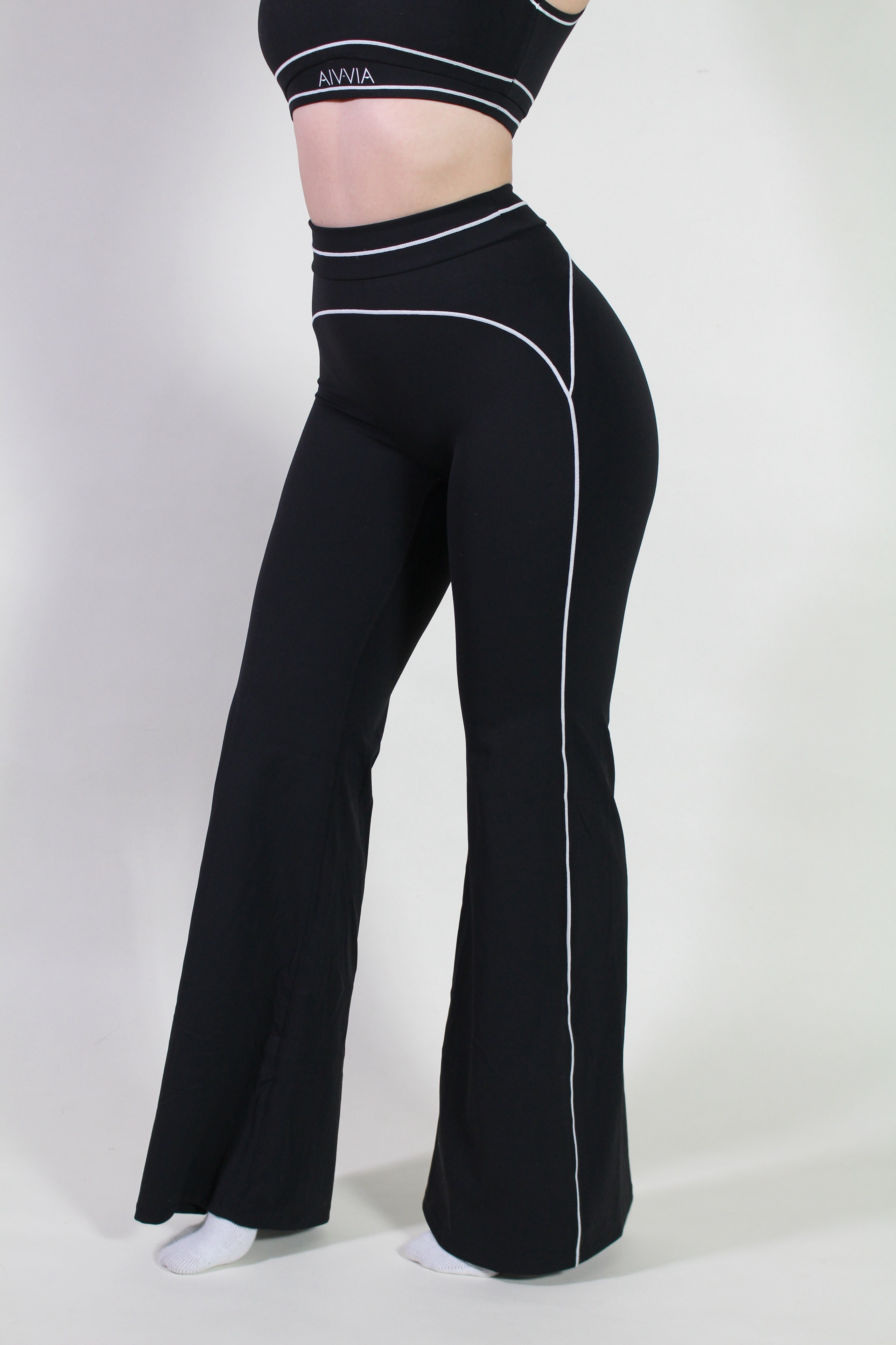 Angled side view highlighting high-waist design and flexible fit of Aivvia Athletics black yoga pants, suitable for active workouts and pilates.