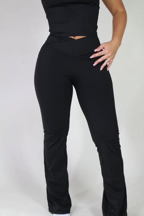 Front-facing view of a woman wearing Aivvia Athletics black sculpt pants, highlighting high-waist crossover waistband, flared leg, and side pockets for gym or everyday activewear.