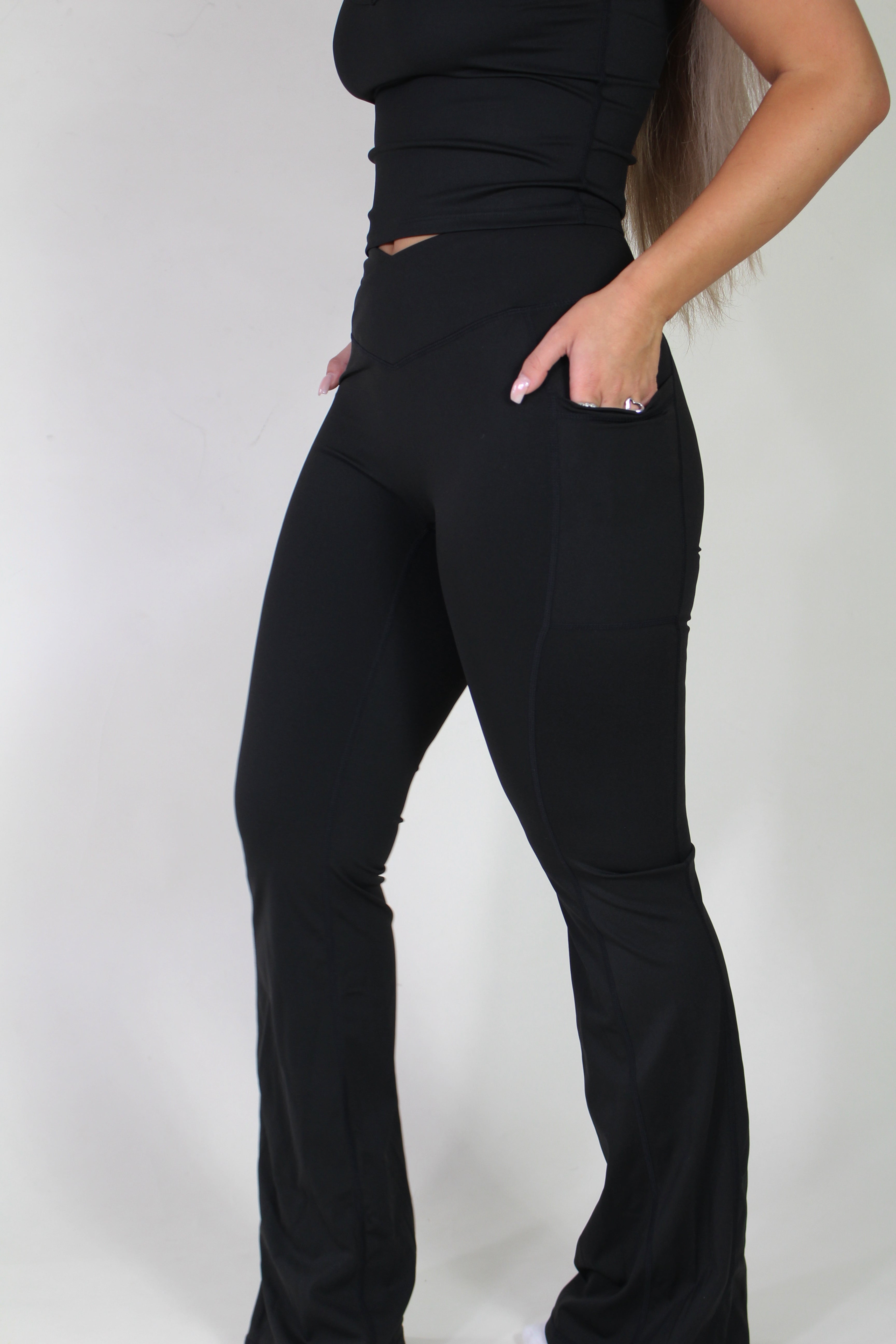 Side profile of Aivvia Athletics black sculpt pants, showcasing flared leg, sculpting fit, and convenient pocket detail.