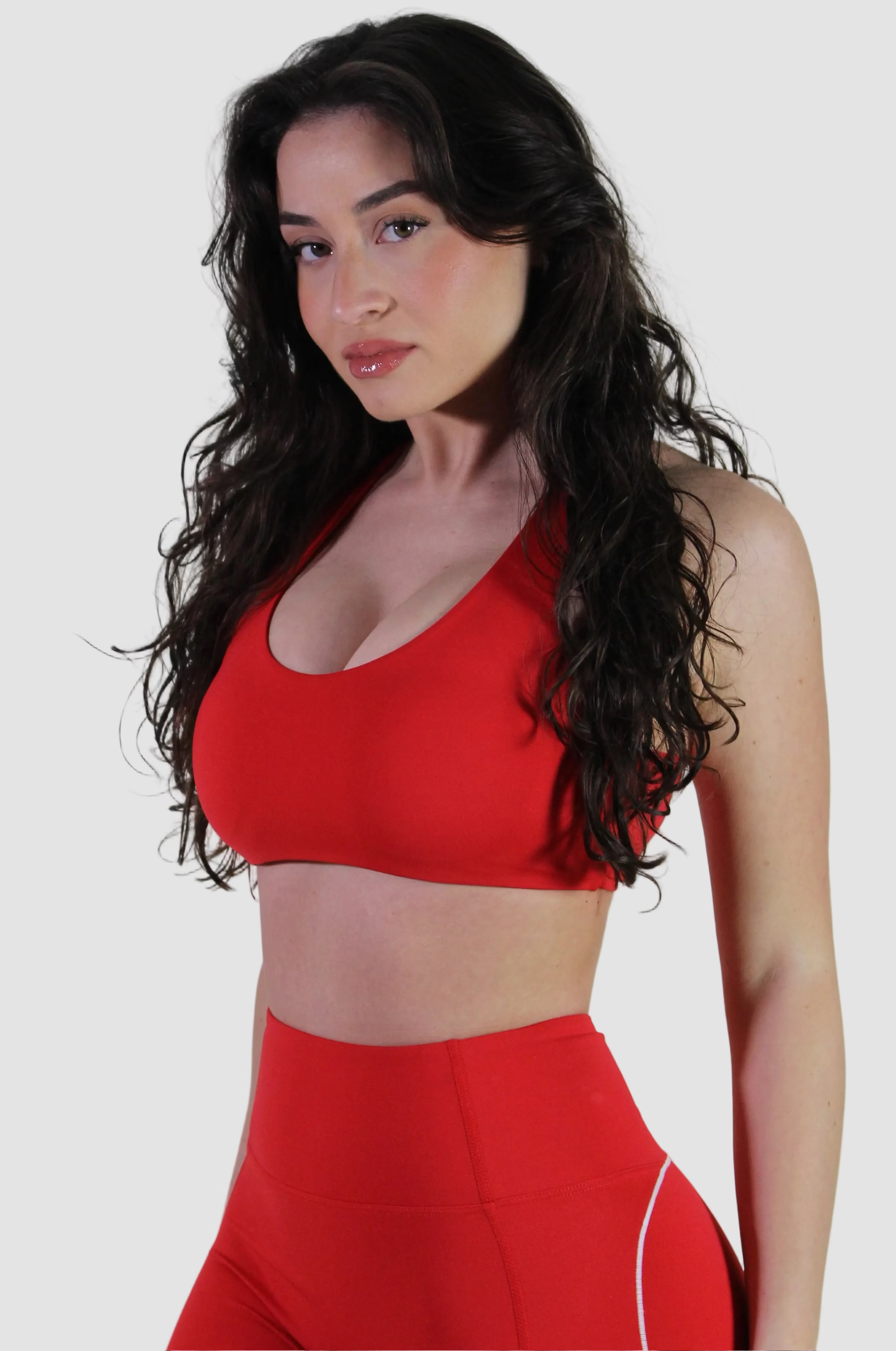 Woman wearing a red sports bra and leggings against a plain background