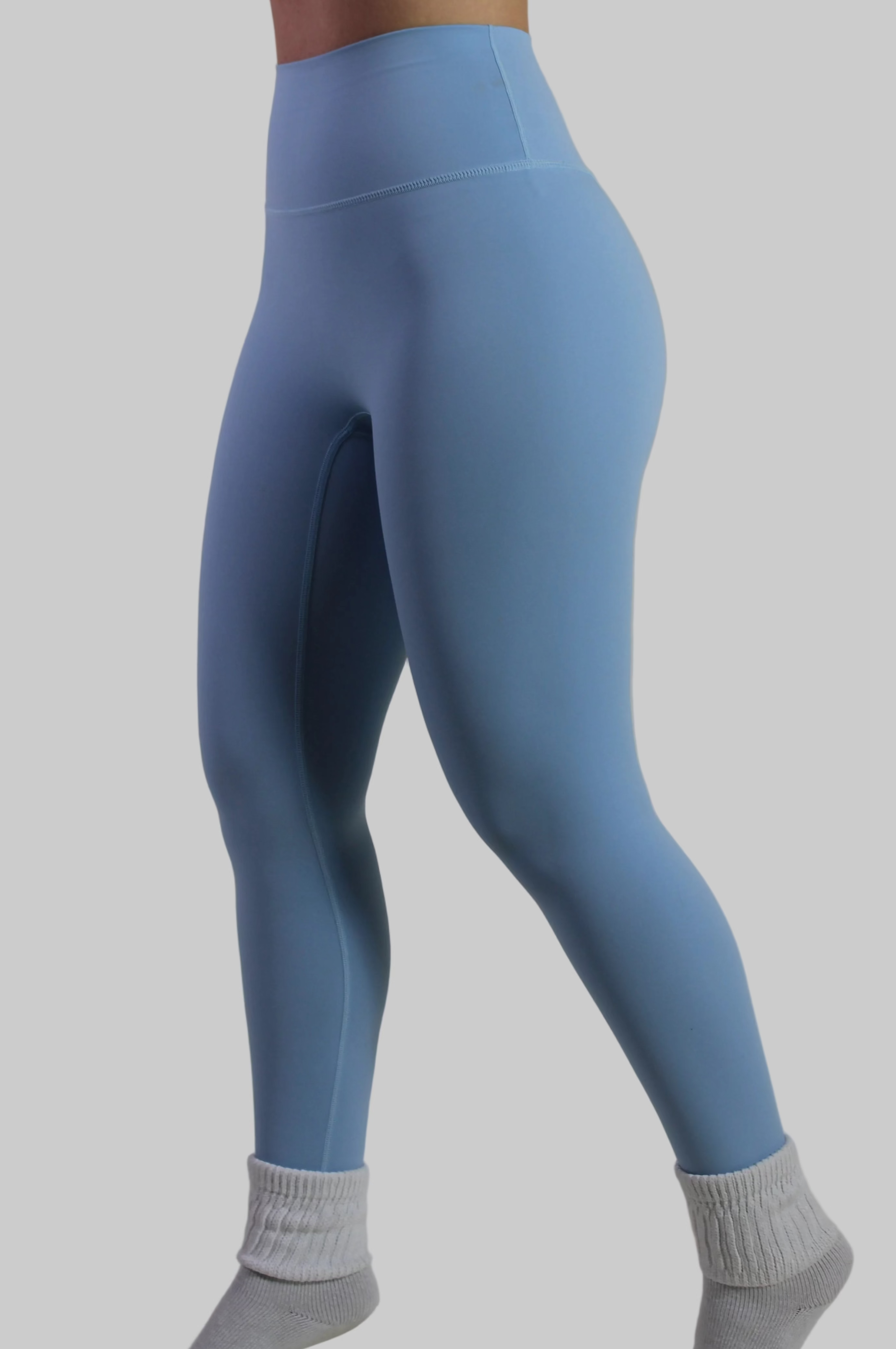 Woman wearing Aivvia Athletics baby blue high-waisted leggings, with smooth seamless front panel for gym and workout.