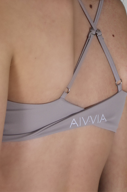 Close-up of light taupe Aivvia Athletics sports bra featuring thin criss-cross straps and back logo detail.