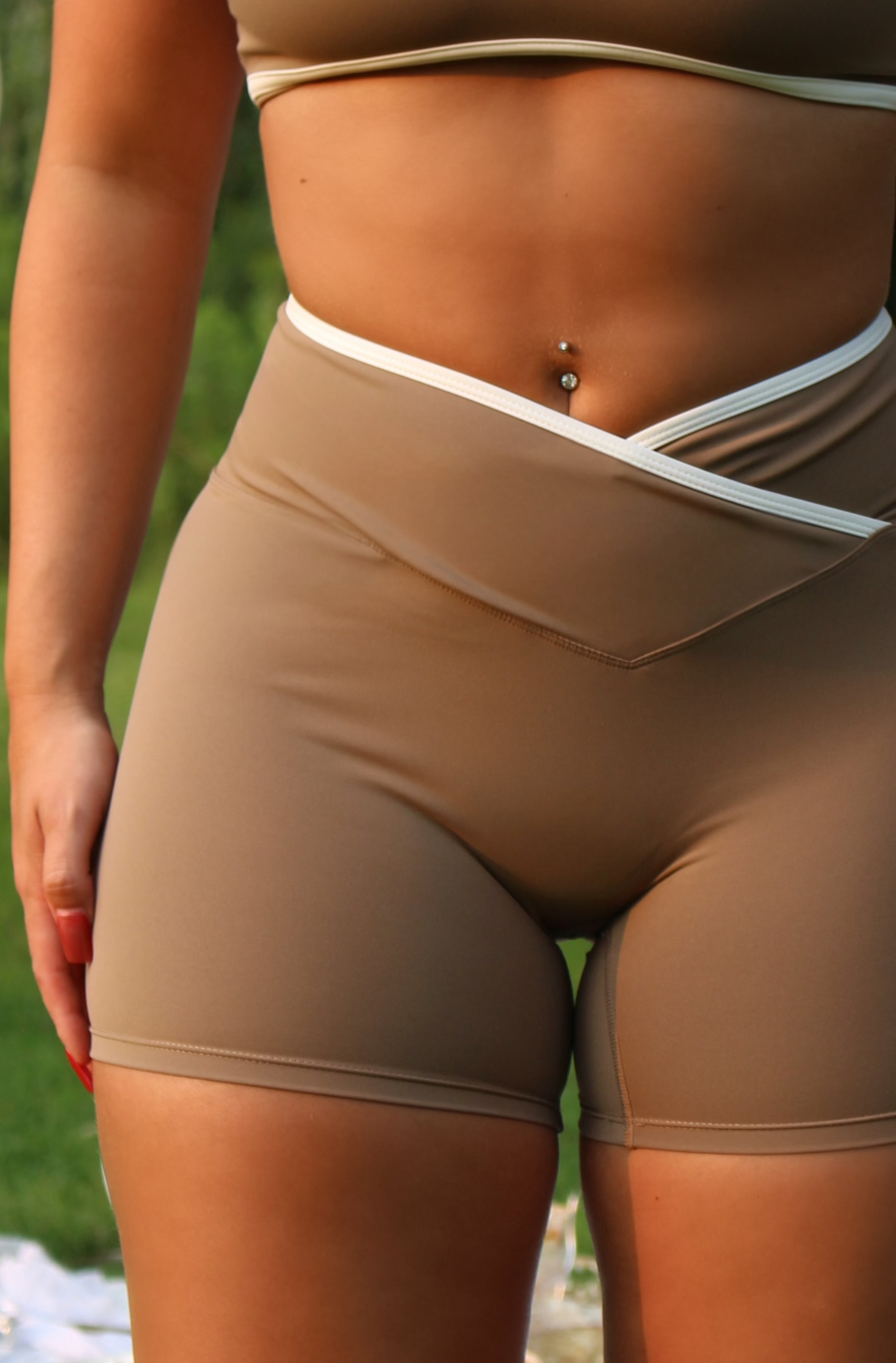 Woman wearing a beige sports bra and shorts set outdoors with balloons and greenery.