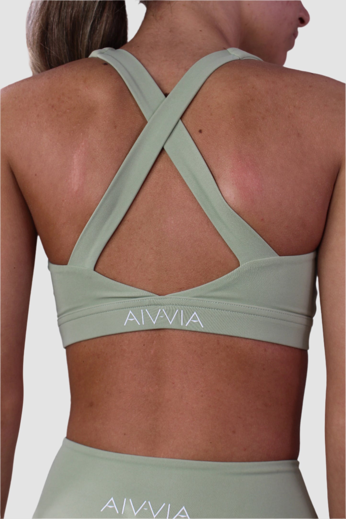 Close-up of Aivvia Athletics sage green sports bra crisscross strap detail and wide elastic underband for stability.