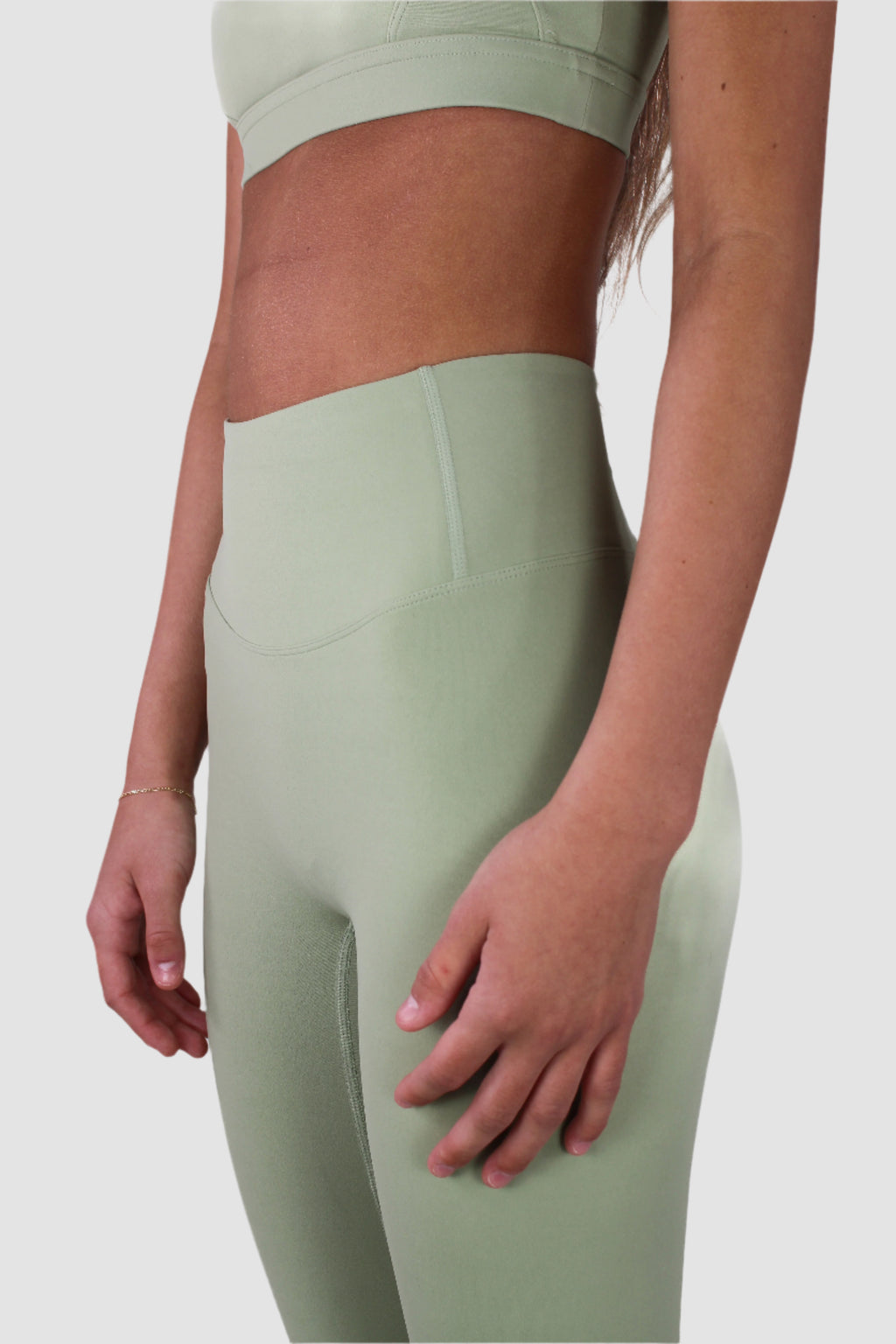 Side profile of woman in sage green Aivvia Aesthetics leggings, highlighting seamless design, body contour, and ankle-length cut.