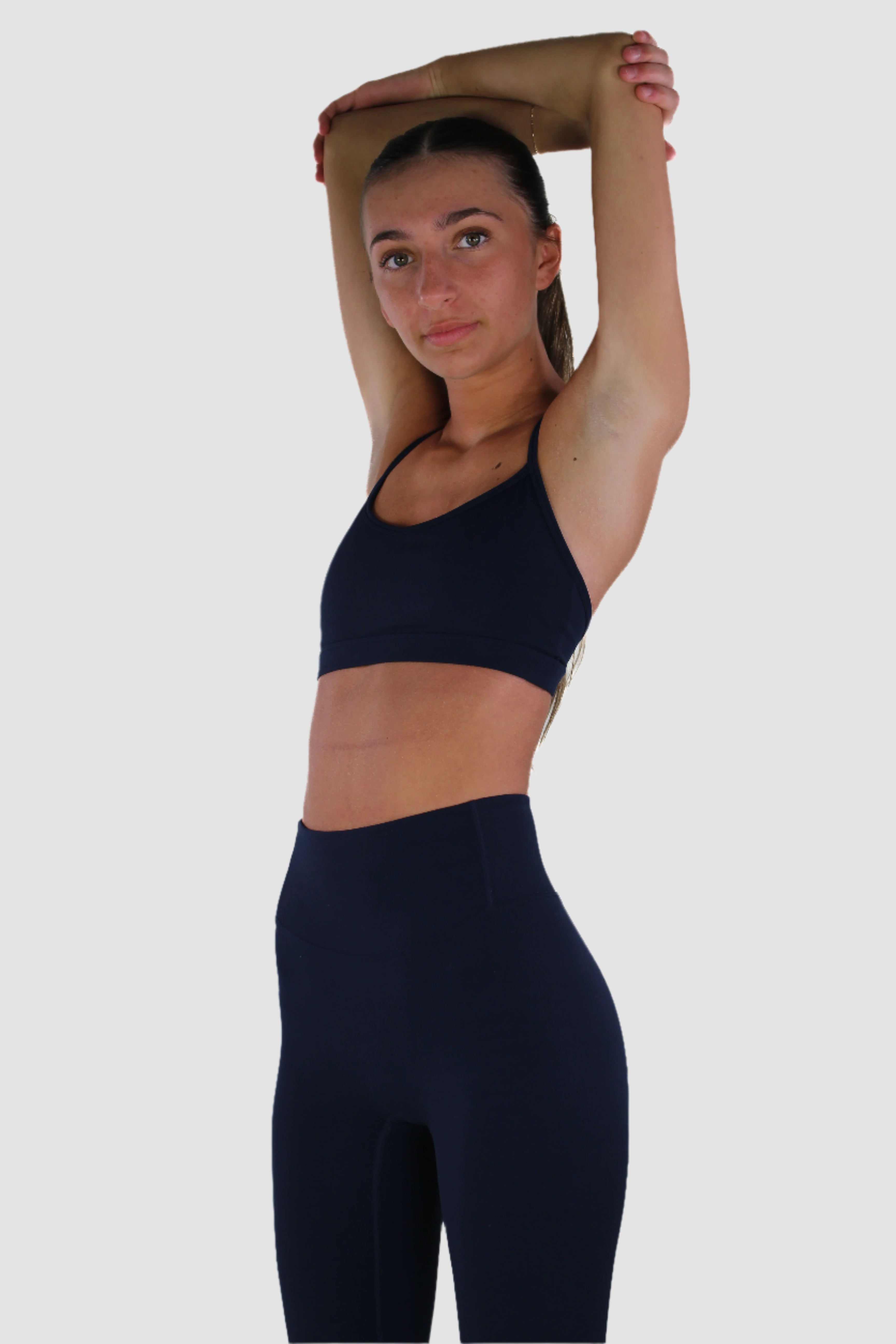 Navy Aivvia Athletics sports bra with thin straps and open back, paired with high-waisted leggings.