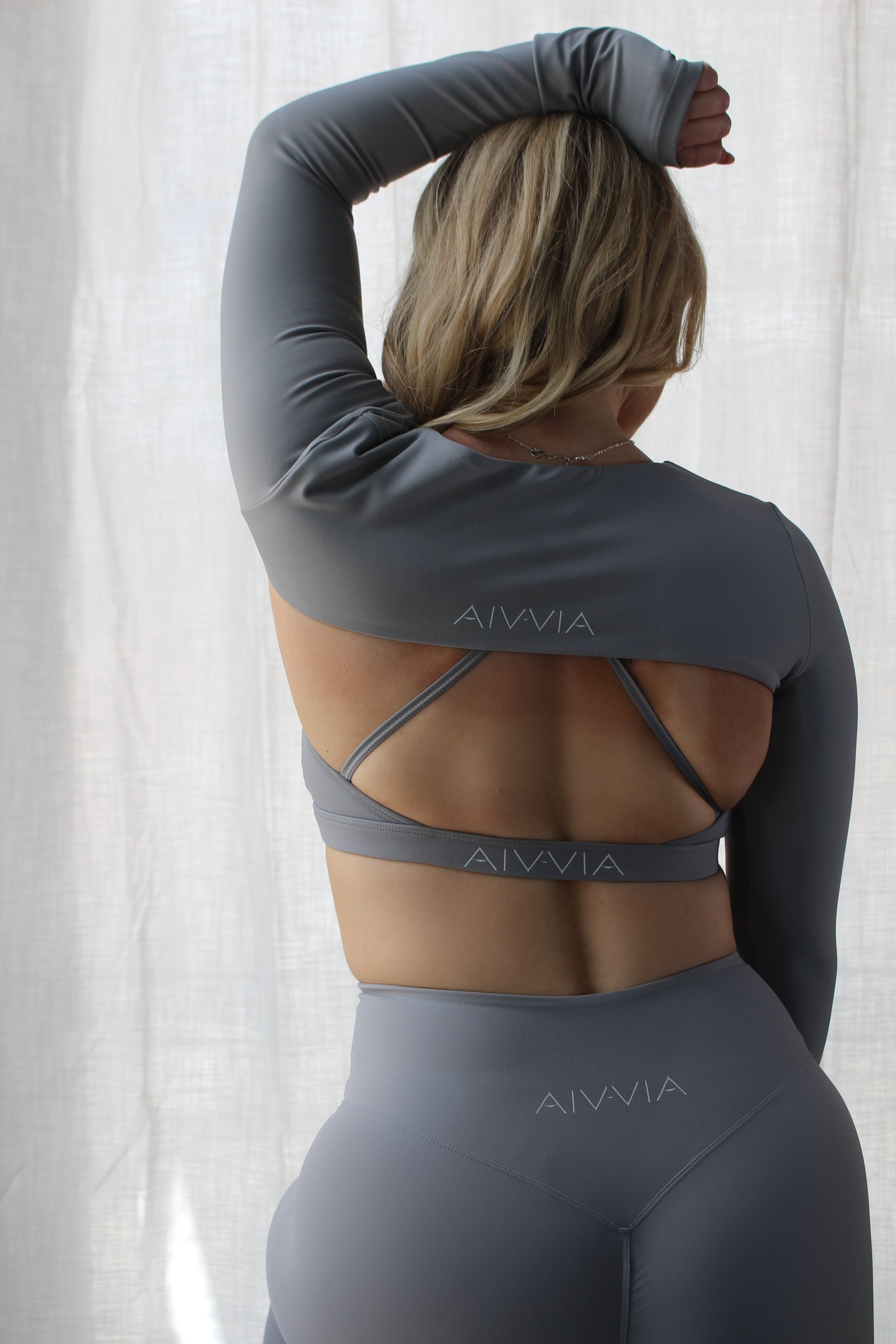 Back view of woman wearing Aivvia Athletics open-back crop top layered over a criss-cross sports bra – modern and breathable gym outfit for women.