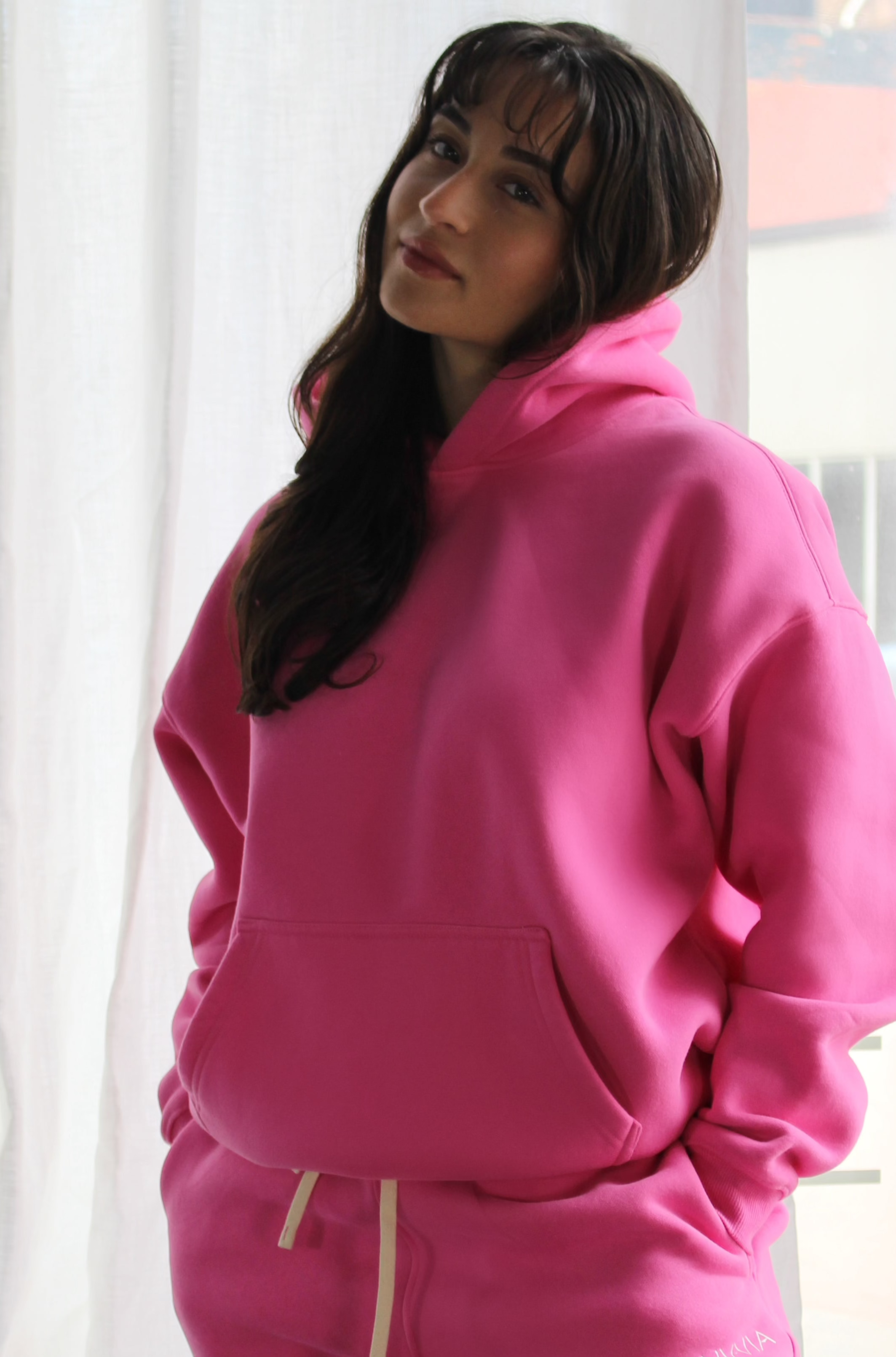 Bold pink Aivvia Athletics hoodie in a relaxed pose; cozy fleece material, drop-shoulder design, and modern loungewear style.