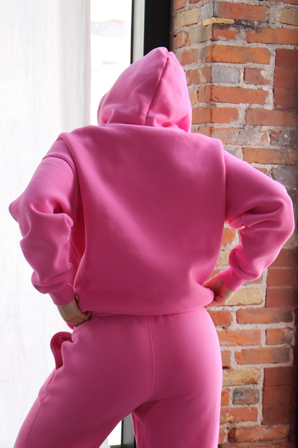 Back view of woman wearing pink hoodie, relaxed fit for workouts or casual wear.