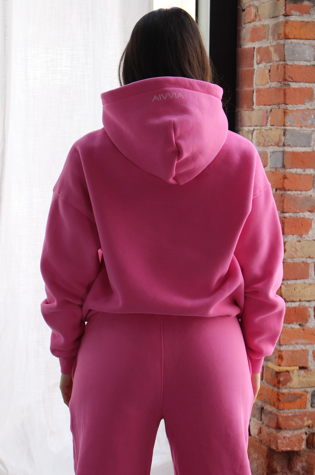 Back view of woman wearing pink hoodie, relaxed athletic fit for layering and movement.