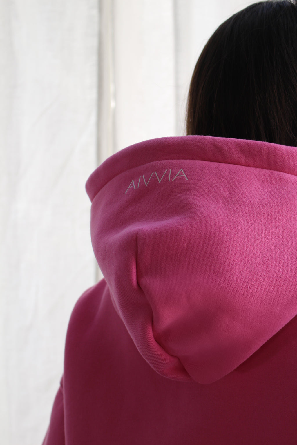 Close-up of hood and upper back of woman wearing pink hoodie with subtle Aivvia logo.