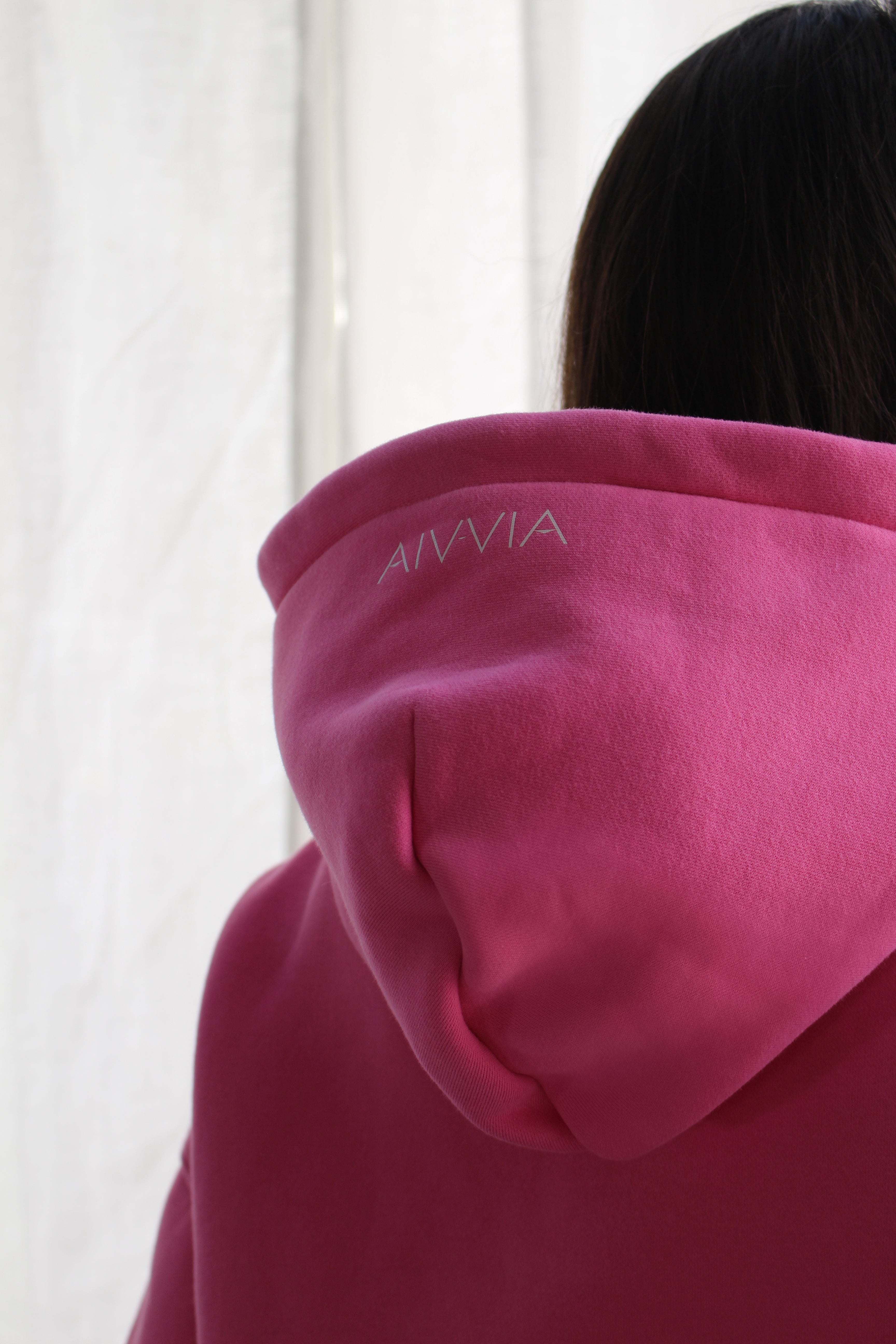 Close-up of hood and upper back of woman wearing pink hoodie with subtle Aivvia logo.