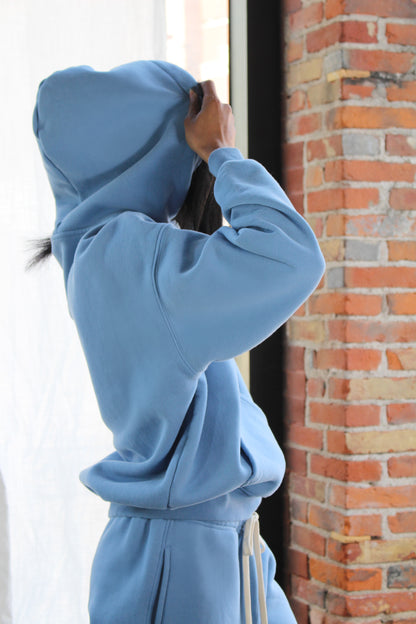 Side profile of woman in Aivvia Athletics light blue hoodie; soft fleece texture with structured hood and drawstring waist.