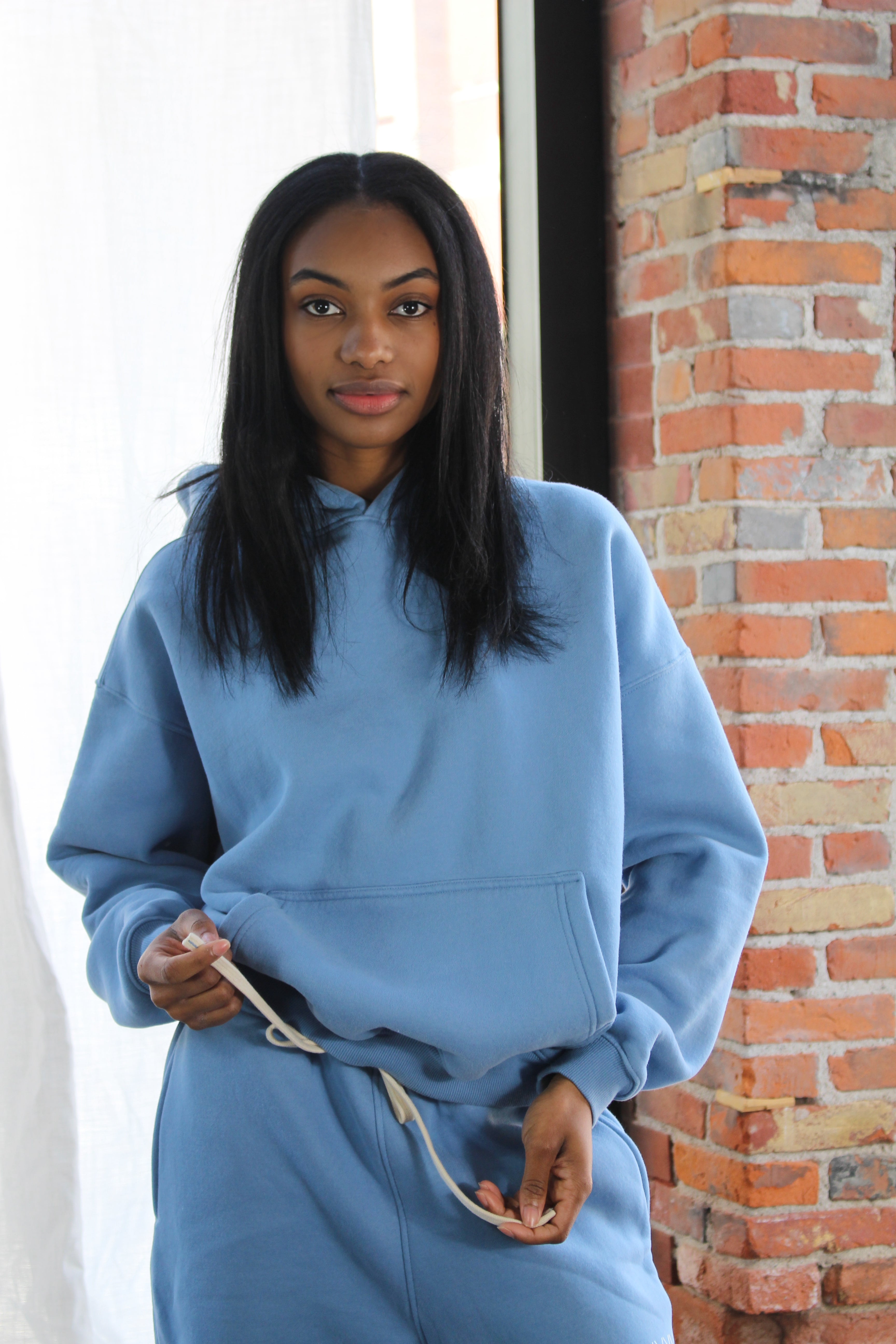 Comfortable light blue Aivvia Athletics hoodie styled with joggers; classic kangaroo pocket and relaxed athletic look.