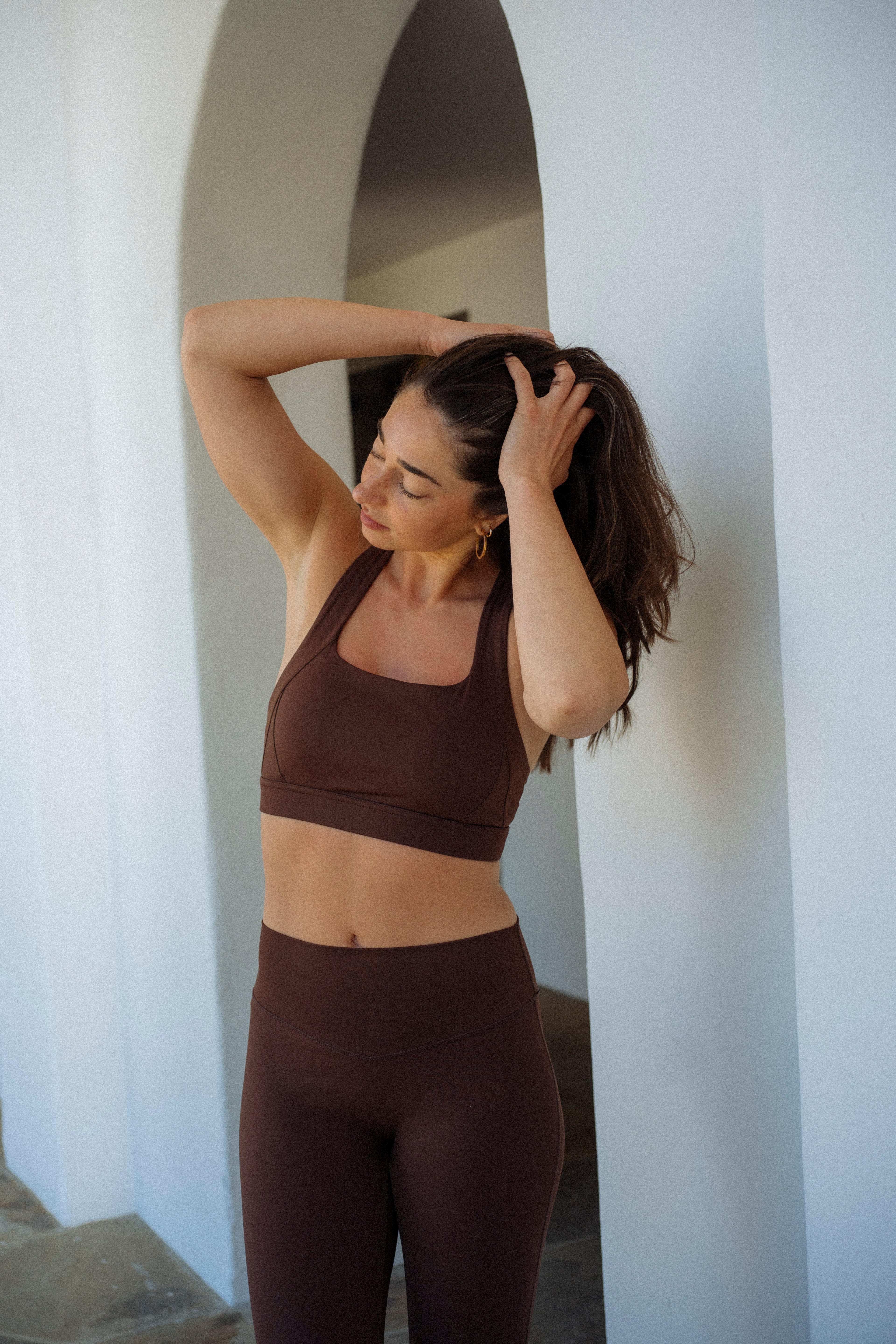 Woman wearing brown Aivvia Athletics sports bra with scoop neckline, paired with matching leggings.