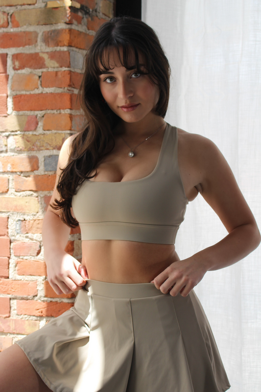 Close-up of woman wearing Aivvia Athletics beige sports bra and pleated active skirt — women’s athletic set ideal for tennis, gym, or athleisure.