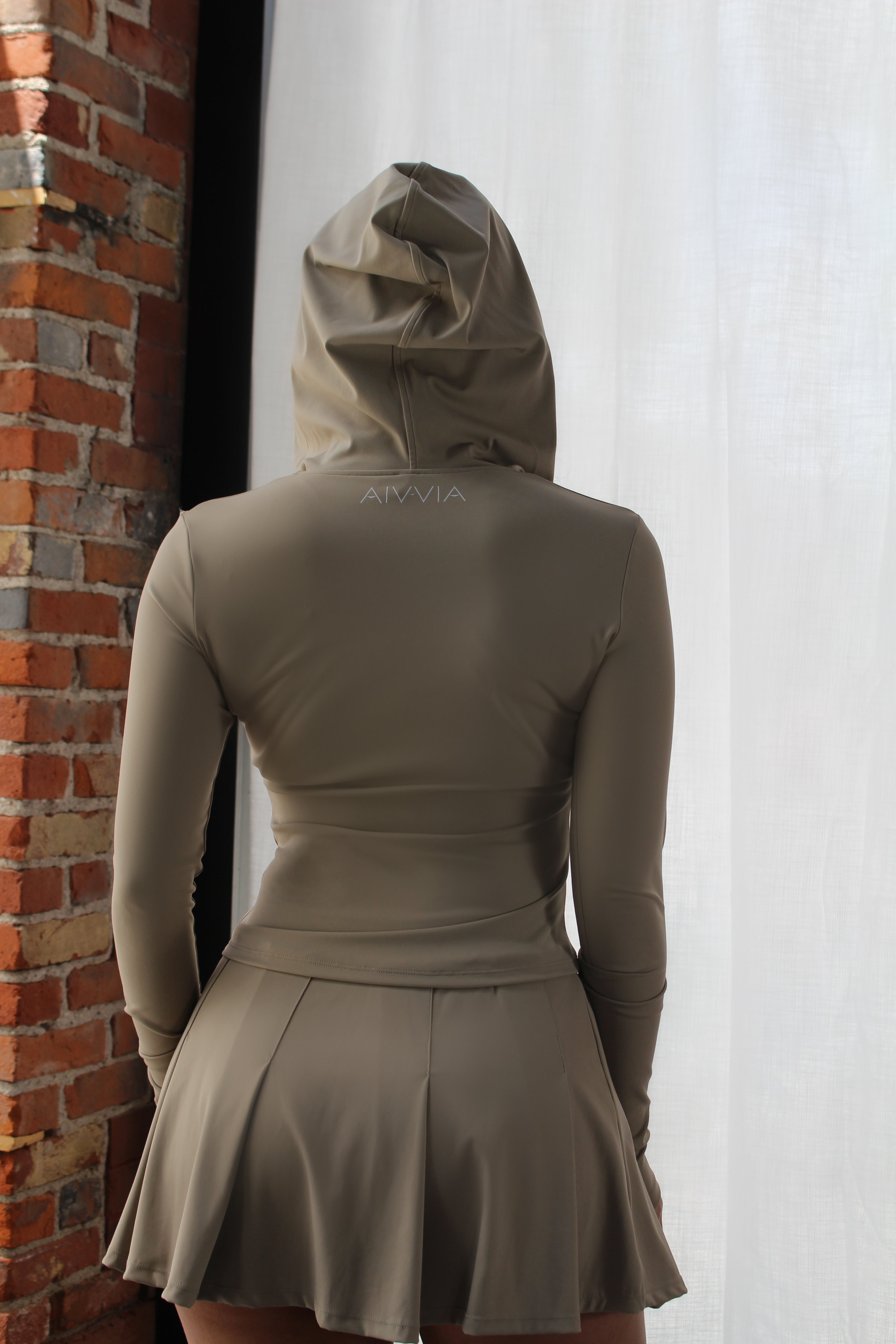 Back view of Aivvia Athletics full zip athletic hoodie and pleated skirt — tailored women’s fitness outerwear with stylish hooded design.