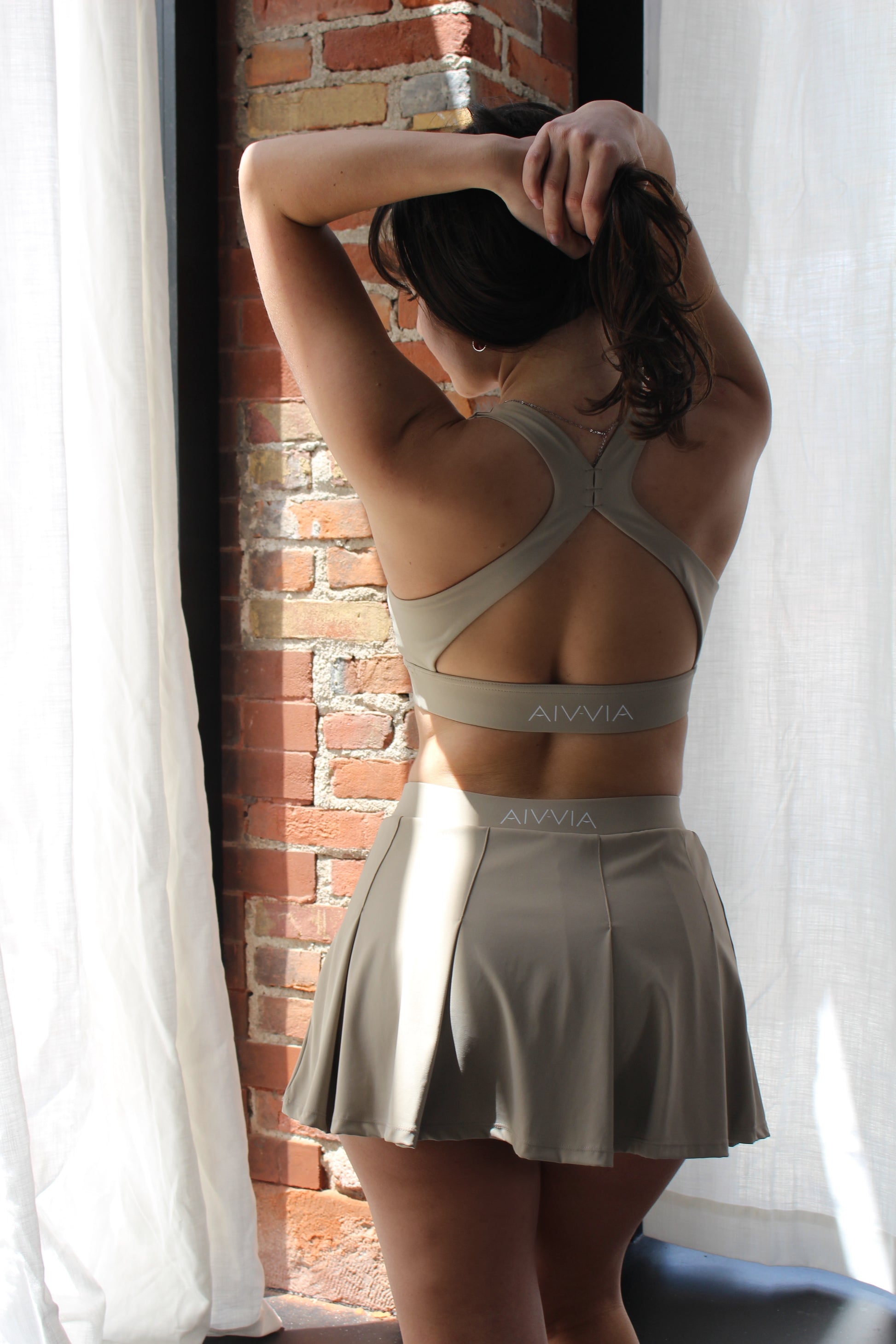 Back view of Aivvia Athletics beige cross-back sports bra and pleated skirt — seamless, breathable women's activewear with stylish open-back design.