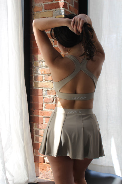 Back view of Aivvia Athletics beige cross-back sports bra and pleated skirt — seamless, breathable women's activewear with stylish open-back design.
