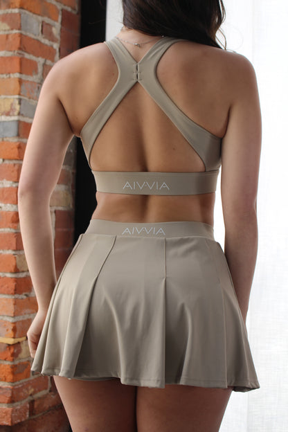 Full back shot of Aivvia Athletics pleated active skirt and cross-back sports bra in beige — women’s coordinated workout set with functional style.