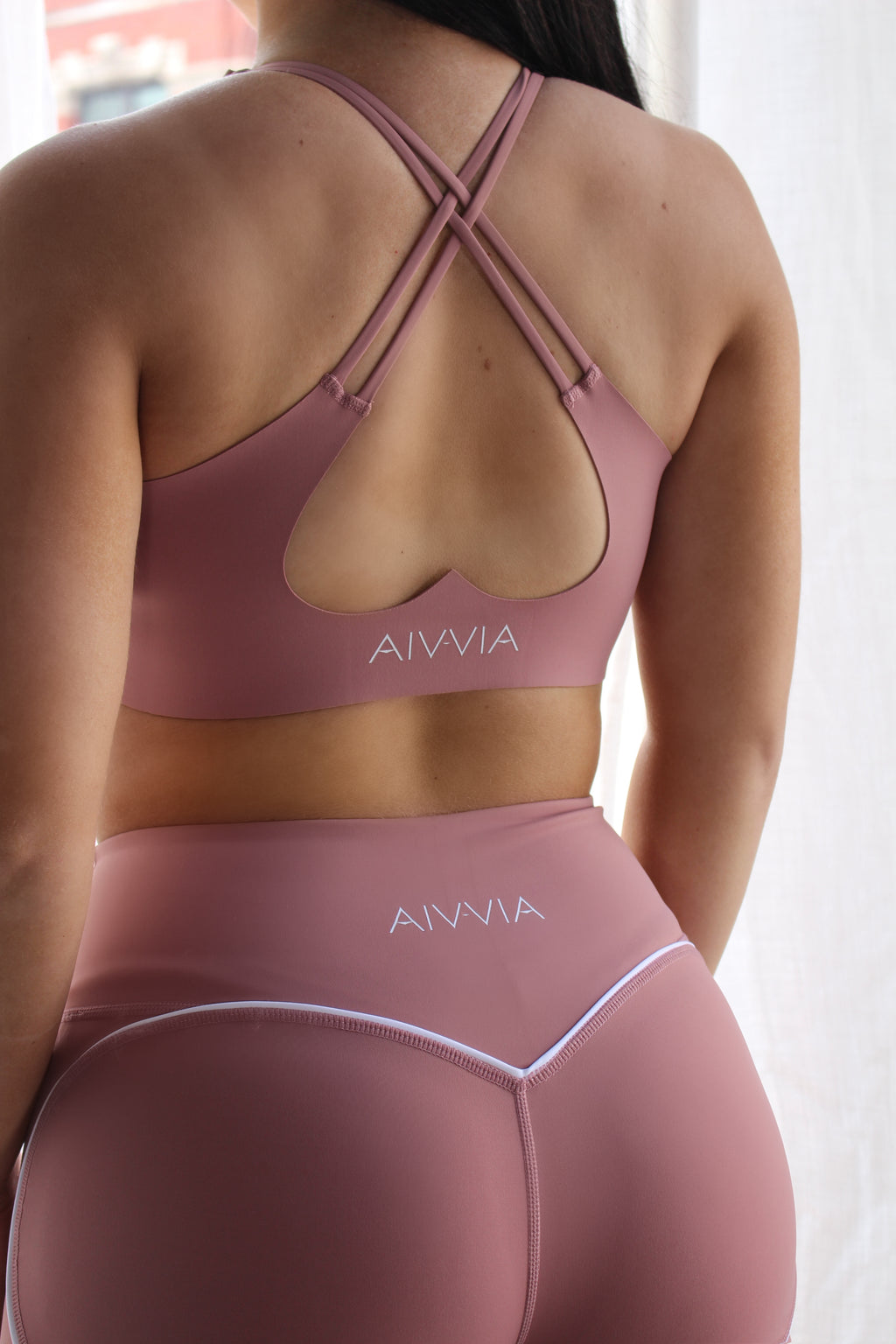 Close-up back view of Aivvia Athletics seamless sports bra in blush pink with crisscross straps and open back support structure.