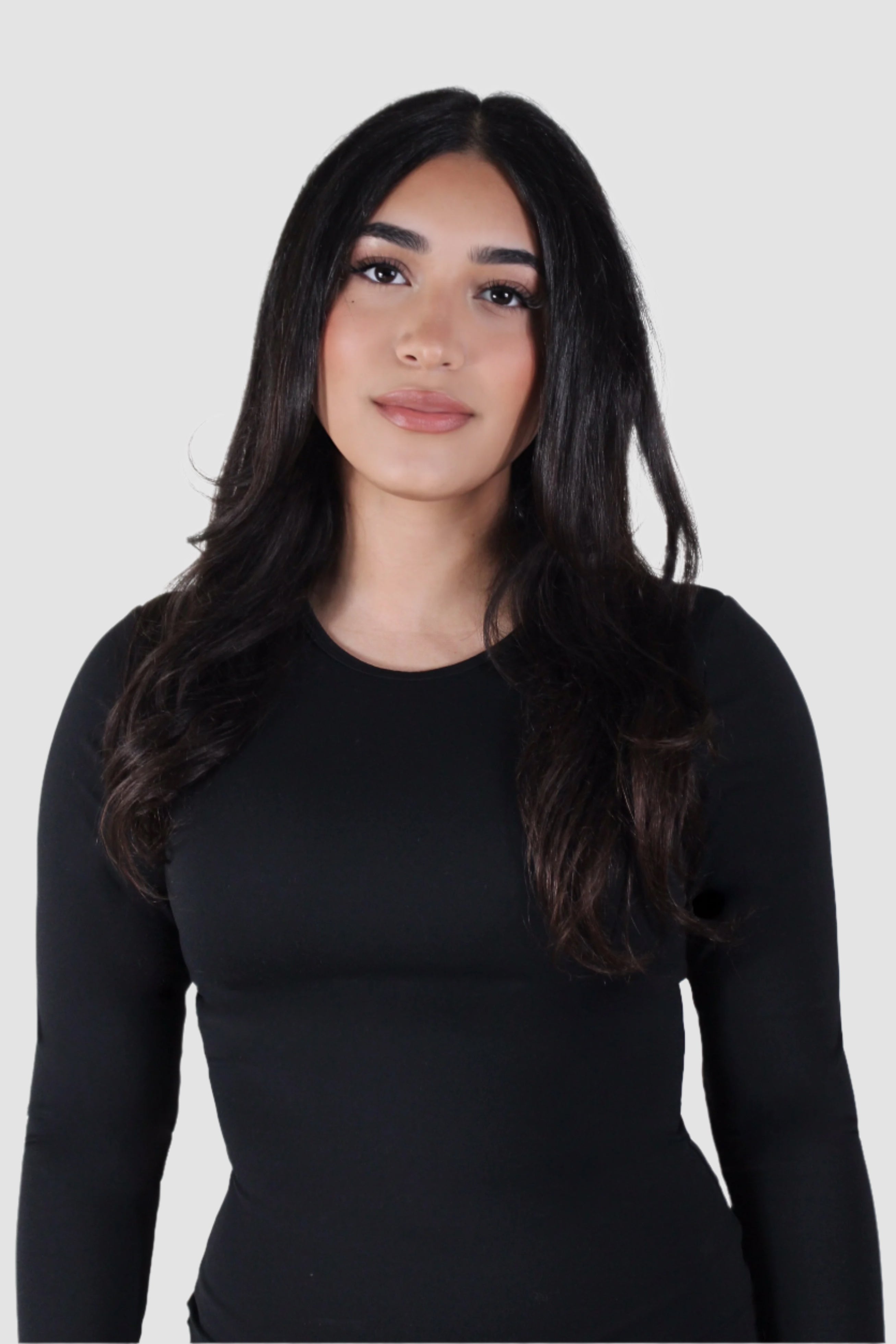Front-facing studio portrait of a woman wearing the Aivvia Athletics Tone Long Sleeve in black — seamless, fitted women’s activewear top with full-length sleeves, ideal for workouts, yoga, or athleisure.